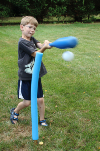 A boy hitting a wiffle ball from a pool noodle tee