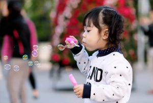 A toddler blowing bubbles in the park.