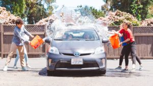 4 teenagers throwing buckets of water on a car